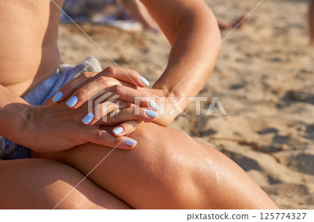 Woman hands on knees with blue manicure on sunny day, beach  125774327