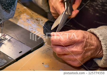 The hands of a tailor cut a piece of fabric with scissors 125774350