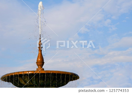 Fountain with a root bowl,shiny transparent liquid,sky with clouds Fountain with a root bowl,shiny transparent liquid,sky with clouds 125774353