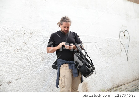 Photographer using smartphone app while leaning on white wall 125774583