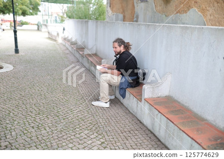 Tourist reading travel guide while sitting on bench in park Tourist reading travel guide while sitting on bench in park 125774629