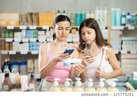 Woman and girl daughter in pharmacy scans QR code on gel for burns Woman and girl daughter in pharmacy scans QR code on gel for burns 125775281