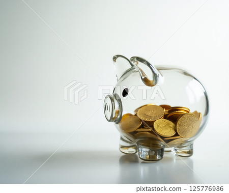 Transparent piggy bank filled with gold coins sits against a simple background symbolizing savings and financial planning Transparent piggy bank filled with gold coins sits against a simple background symbolizing savings and financial planning 125776986