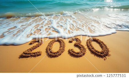 Waves softly wash over sandy beach with 2030 marked in the sand on a sunny day 125777531