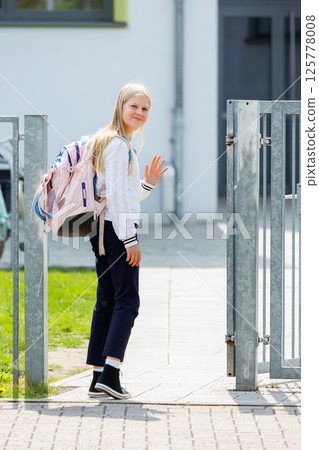 Portrait german cute blonde kid teenager school girl wear white jacket gymnasium uniform enjoy walking city street after lesson study end. Female child person student at campus college area outside 125778008