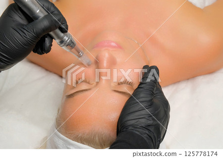 Microneedle RF lifting procedure. A cosmetologist performs a facial rejuvenation procedure on a woman. Hardware cosmetology. Microneedle RF lifting procedure. A cosmetologist performs a facial rejuvenation procedure on a woman. Hardware cosmetology. 125778174