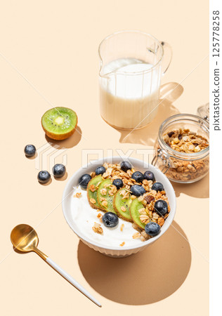 Natural yogurt with granola, kiwi and blueberries in a bowl on a beige background. 125778258