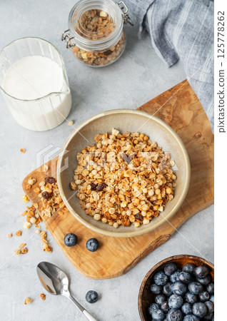 Homemade baked granola or muesli in a bowl on a wooden board on a light background Homemade baked granola or muesli in a bowl on a wooden board on a light background 125778262