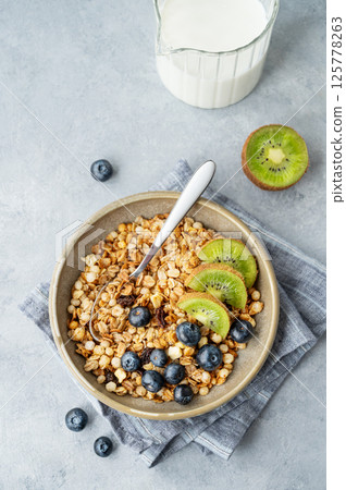 Homemade baked granola or muesli in a bowl with kiwi and blueberries on a light background 125778263