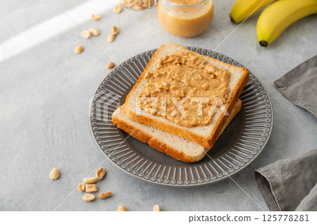 Peanut butter toast on a plate on a light background with banana and morning shadow. Peanut butter toast on a plate on a light background with banana and morning shadow. 125778281