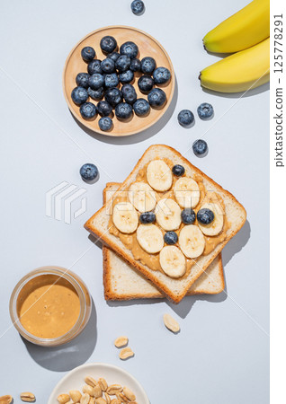 Flat lay of peanut butter toast on with banana, blueberry and nuts on a blue background. 125778291