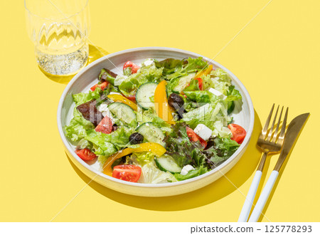 Vegetable salad with lettuce, olives and feta cheese on yellow background 125778293