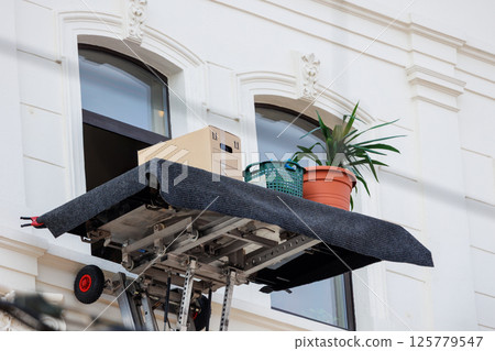 Mover service lifting ladder cargo crane platform cardboard box plant pot city street. Retractable furniture elevator machine car pickup truck rental company for relocation and house moving delivery 125779547