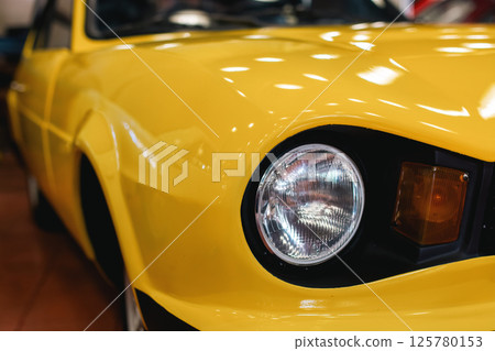 Close up of a headlight of an classic yellow car Close up of a headlight of an classic yellow car 125780153