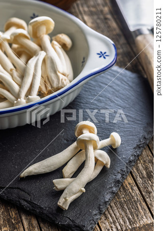 Raw white shimeji mushrooms on cutting board. 125780211