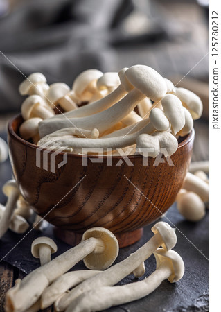 Raw white shimeji mushrooms in bowl on cutting board. 125780212