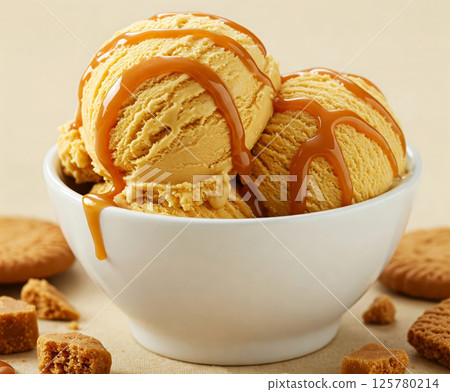 Close-up of a white bowl filled with three scoops of caramel creamy ice cream, garnished with a caramel and cookies. 125780214