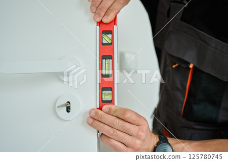 Carpenter Checking Door Alignment with Spirit Level 125780745