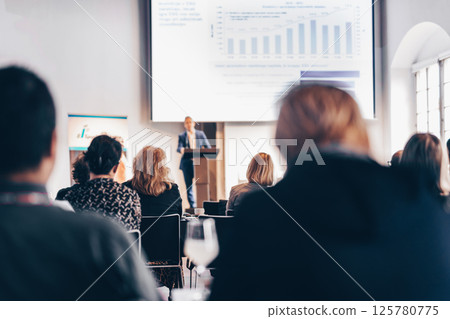 Speaker giving a talk in conference hall at business event. Rear view of unrecognizable people in audience at the conference hall. Business and entrepreneurship concept 125780775