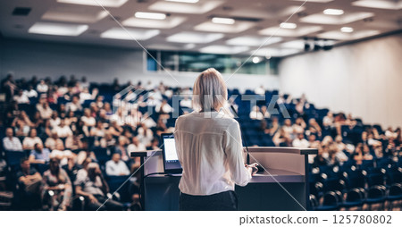 Female speaker giving a talk on corporate business conference. Unrecognizable people in audience at conference hall. Business and Entrepreneurship event Female speaker giving a talk on corporate business conference. Unrecognizable people in audience at conference hall. Business and Entrepreneurship event 125780802