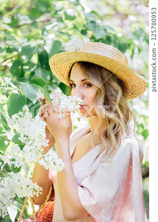 Woman in straw hat and pink dress gently smelling white lilac flowers in lush green garden on a sunny spring day Woman in straw hat and pink dress gently smelling white lilac flowers in lush green garden on a sunny spring day 125780953