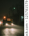 An old school bus drives down a foggy street at night 125781579