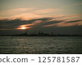 A stunning sunset lights up the water with a city skyline behind 125781587