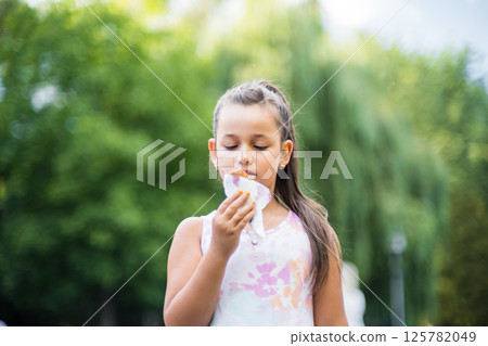 A cute child enjoys a delicious ice cream cone during the summer. Childs with ice cream on a walk in the city park. A cute child enjoys a delicious ice cream cone during the summer. Childs with ice cream on a walk in the city park. 125782049