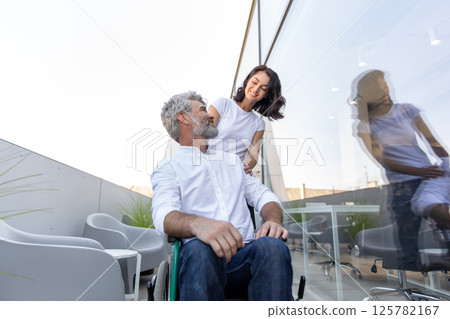 Dark-haired woman carrying a wheelchair of her husband 125782167