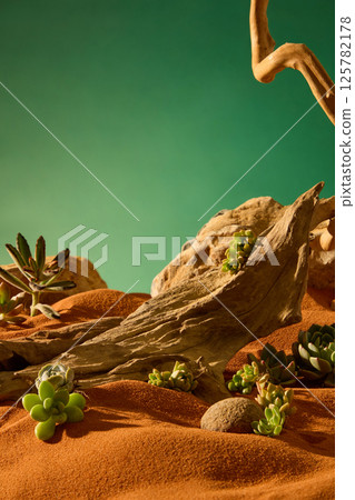 Vertical photo of ancient tree bark with long ridges and sharp edges. Succulents and desert plants grow on the sand, around the round pebbles. Large boulders in the behind rise up like mountains. 125782178