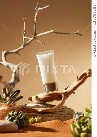 A cosmetic tube with a silver metal cap stood tilted on a brown tree trunk, with a rough rock underneath. The dry and leafless tree still grew, its top pointing to the sky, surrounded by succulents. A cosmetic tube with a silver metal cap stood tilted on a brown tree trunk, with a rough rock underneath. The dry and leafless tree still grew, its top pointing to the sky, surrounded by succulents. 125782185