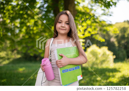 School girl walking outside in green summer park with books in hands 125782258