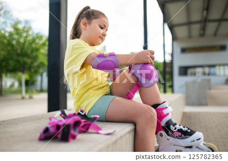 Little female skater preparing with protection gear for roller-skating outside Little female skater preparing with protection gear for roller-skating outside 125782365