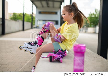 Little female skater adjusting protective gear on knees before skating 125782375
