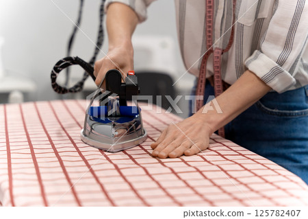 Close up of fashion designer doing ironing in her studio 125782407