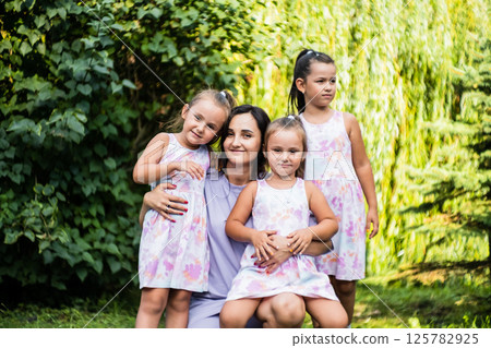 The three sisters cuddle up to their mom, their faces glowing with happiness. The little twins rest their heads on her shoulders. The three sisters cuddle up to their mom, their faces glowing with happiness. The little twins rest their heads on her shoulders. 125782925
