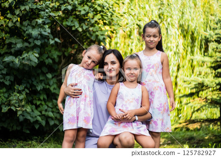 The three sisters cuddle up to their mom, their faces glowing with happiness. The little twins rest their heads on her shoulders. The three sisters cuddle up to their mom, their faces glowing with happiness. The little twins rest their heads on her shoulders. 125782927