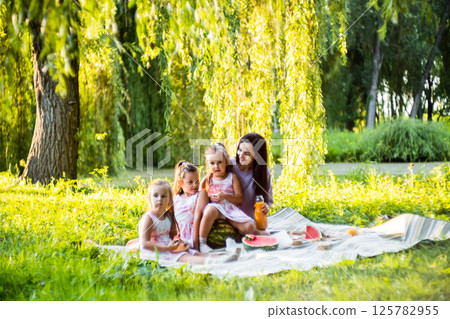 The picnic is full of joy as the girls enjoy their treat. The twins hold their slices carefully, giggling. The picnic is full of joy as the girls enjoy their treat. The twins hold their slices carefully, giggling. 125782955