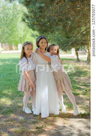 A little lady in a long ivory dress stands at the center of attention. Two younger girls gently hug the older child, emphasizing the family bond. 125783077
