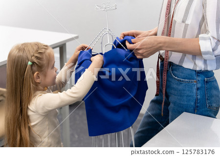 Sweet little girl helping her mom in a sewing salon Sweet little girl helping her mom in a sewing salon 125783176