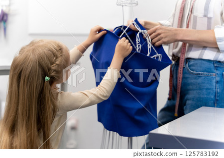 Sweet little girl helping her mom in a sewing salon Sweet little girl helping her mom in a sewing salon 125783192