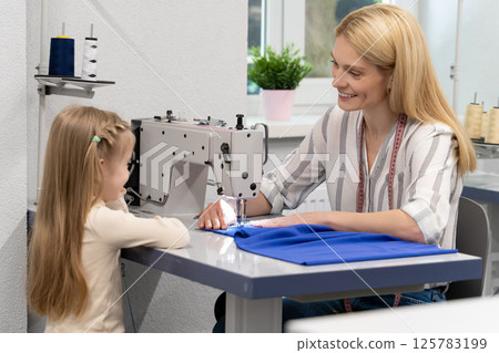 Blonde long-haired female dress designer in her studio with her daughter Blonde long-haired female dress designer in her studio with her daughter 125783199