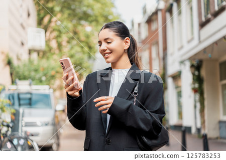 Stylish young woman exploring a new neighborhood, using her phone for local guides, mobile banking, and mindful check-ins Stylish young woman exploring a new neighborhood, using her phone for local guides, mobile banking, and mindful check-ins 125783253