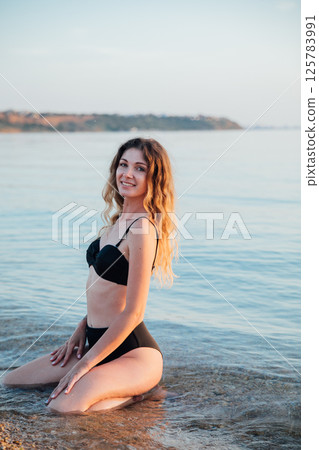 Woman in swimsuit sunbathing and swimming on the beach by the sea 125783991