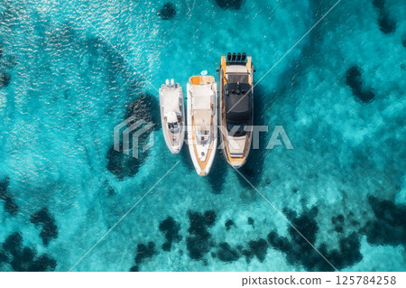 Aerial view of three yachts on transparent azure water Aerial view of three yachts on transparent azure water 125784258