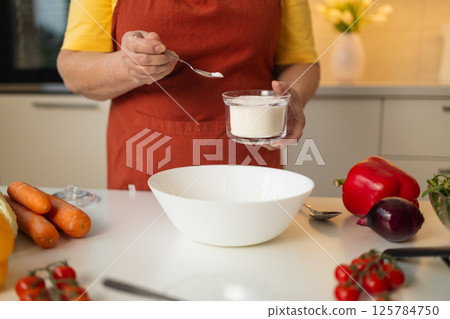 Senior Woman Adding Sugar to a Bowl for Cooking in the Kitchen Senior Woman Adding Sugar to a Bowl for Cooking in the Kitchen 125784750