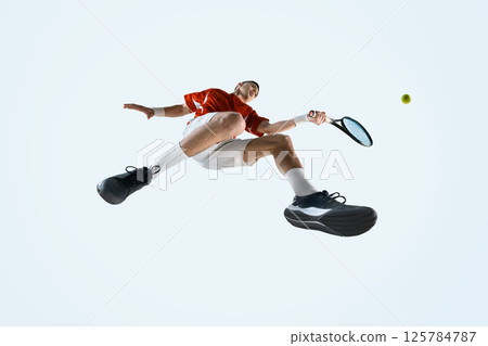 Bottom view of focused young man, tennis player in uniform in motion with ball and racket, during intense game moment 125784787