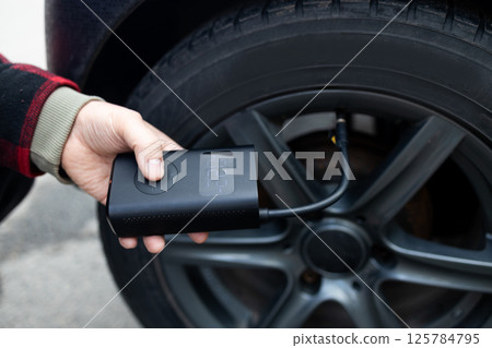 Close up of man hand holds a wireless portable air pump for inflating car tires. Self service, maintenance and safety.  125784795