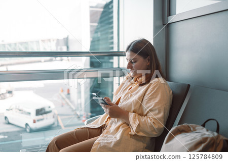 Young woman in the airport terminal using smartphones while waiting for her flight. 125784809