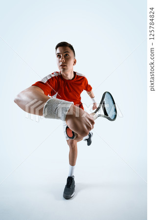 Tennis player prepares powerful forehand shot during dynamic match moment against white studio background. 125784824